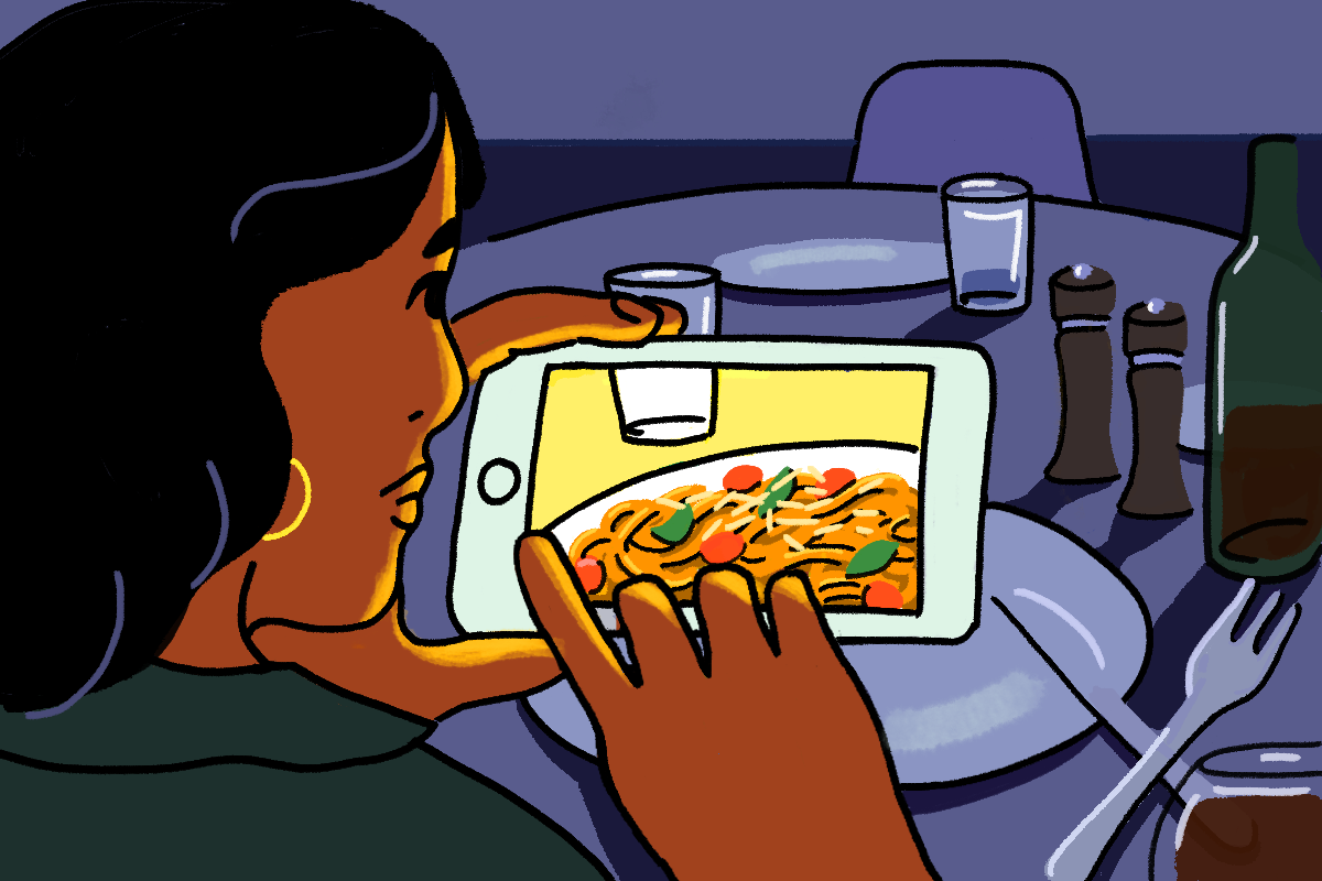 An illustration of women sitting at a dining table taking a photo of her food on a her mobile phone. The woman has black flowing hair and a green collared shirt on.